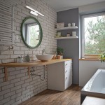 Biały kinkiet LED Splash IP44, umieszczony nad umywalką w łazience. Oświetlenie ma prostokątny kształt i jest zamontowane na ścianie z białej cegły, obok okrągłego lustra w zielonej ramie. W tle widoczne półki z dekoracjami.