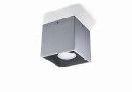 Szara lampa sufitowa 1-punktowa Quad o kwadratowym kształcie. Wykonana z matowego metalu, z widoczną oprawą świetlną na spodzie. Zainstalowana w pozycji wiszącej, z widocznymi śrubami mocującymi. Tło obrazka jest jasne.