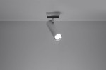 Biała lampa sufitowa (spot) Direzione, 1-punktowa, z cylindrycznym kloszem. Ujęcie z dołu, lampa zamontowana na suficie, emitująca światło. Prosty design, harmonizujący z minimalistycznym wnętrzem. Tło szare, bez dodatkowych elementów.