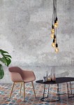 Lampa wisząca Fix Multiple 7-punktowa w kolorze czarnym, z siedmioma żarówkami w stylowych oprawach. Zawieszona na długich, czarnych przewodach, tworzy efektowną iluminację. Tło w odcieniach szarości, z kolorową podłogą i nowoczesnymi meblami.
