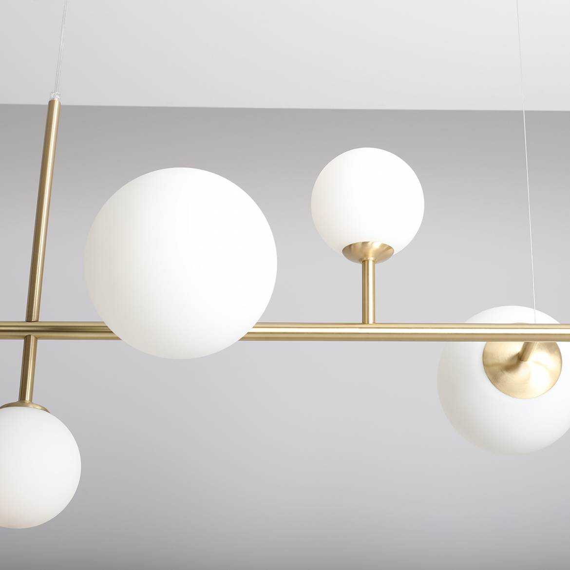 Lampa wisząca Dione 6-punktowa w kolorze mosiądzu, z białymi, okrągłymi kloszami z matowego szkła. Produkt zawieszony na cienkich linkach, z widocznym wykończeniem metalowym, w minimalistycznym stylu.