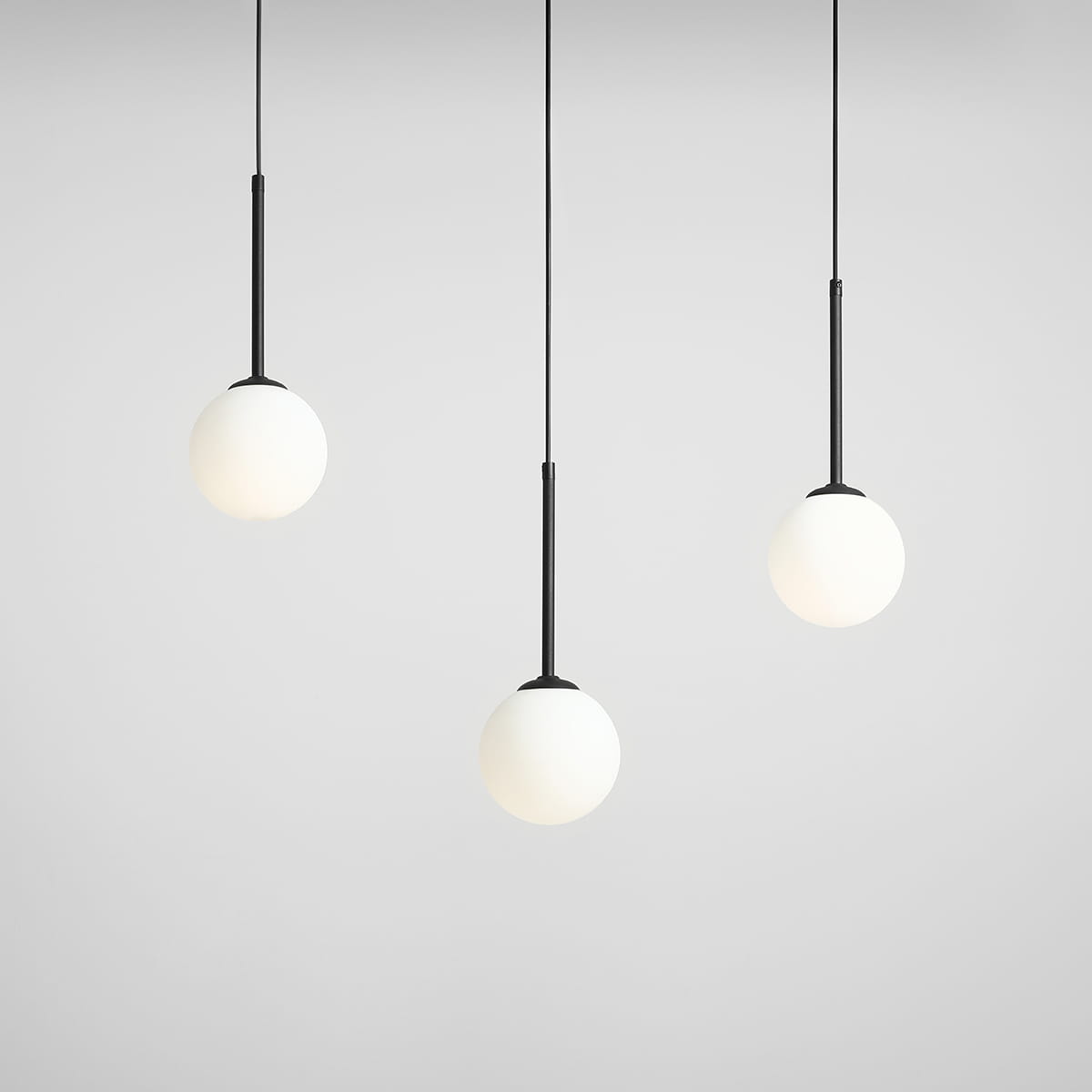 Lampa wisząca Bosso 3-punktowa w kolorze czarnym, z trzema białymi, okrągłymi kloszami, zawieszona na cienkich czarnych linkach. Klosze mają matową powierzchnię, a całość prezentuje się minimalistycznie na jasnym tle.
