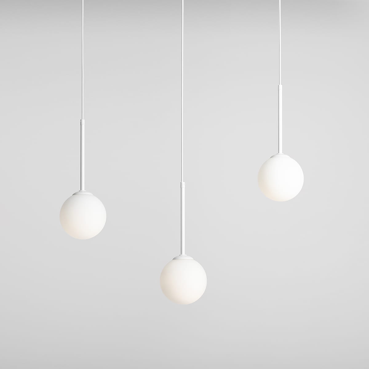 Lampa wisząca Bosso 3-punktowa, biała, składająca się z trzech okrągłych kloszy zawieszonych na cienkich białych przewodach. Klosze mają matową powierzchnię, a całość umieszczona jest na jasnym tle.