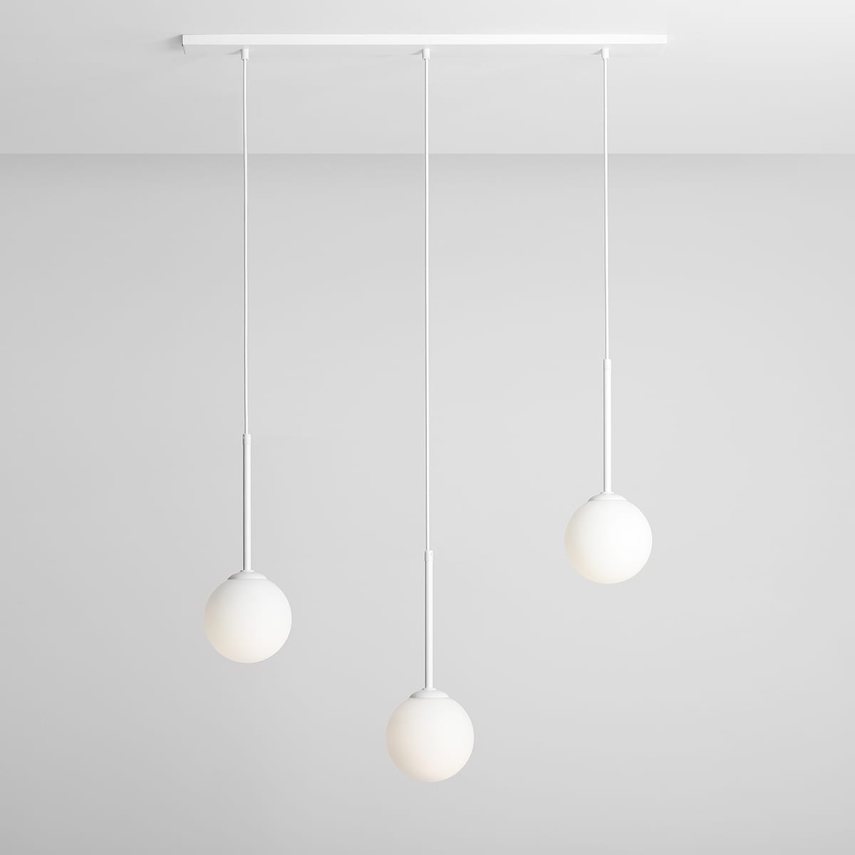 Lampa wisząca Bosso 3-punktowa w kolorze białym, zawieszona na białym stelażu. Składa się z trzech okrągłych kloszy z matowego szkła, zwisających na cienkich linkach. Produkt umieszczony na jednolitym, jasnym tle.