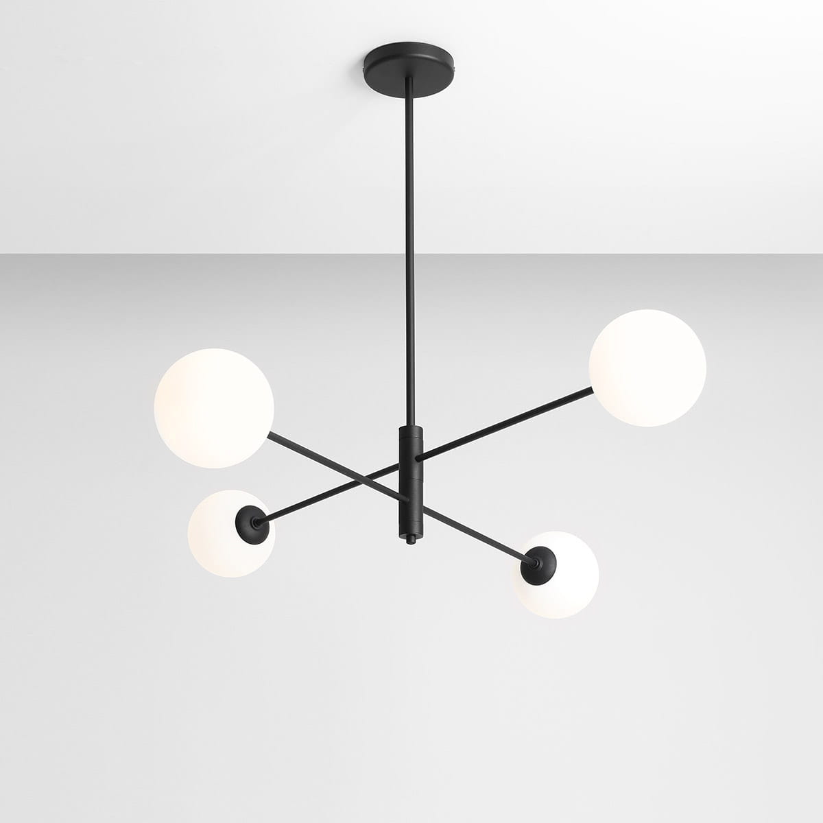 Czarna lampa wisząca Homme z czterema okrągłymi kloszami w białym kolorze, umieszczona na cienkich, prostych ramionach. Ujęcie z góry, pokazujące zawieszenie na suficie oraz symetryczny układ źródeł światła. Tło jasnoszare.