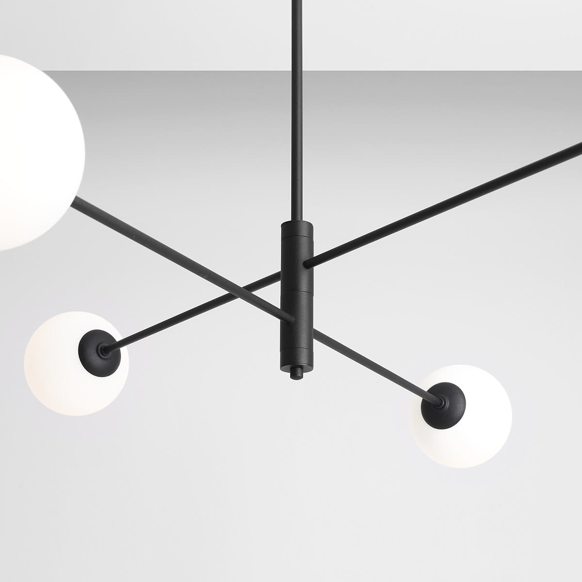 Czarna lampa wisząca 4-punktowa Homme z białymi, okrągłymi kloszami. Widok z dołu, ukazujący centralny element mocujący oraz rozłożone ramiona. Prosta, nowoczesna konstrukcja, umieszczona na jednolitym tle.