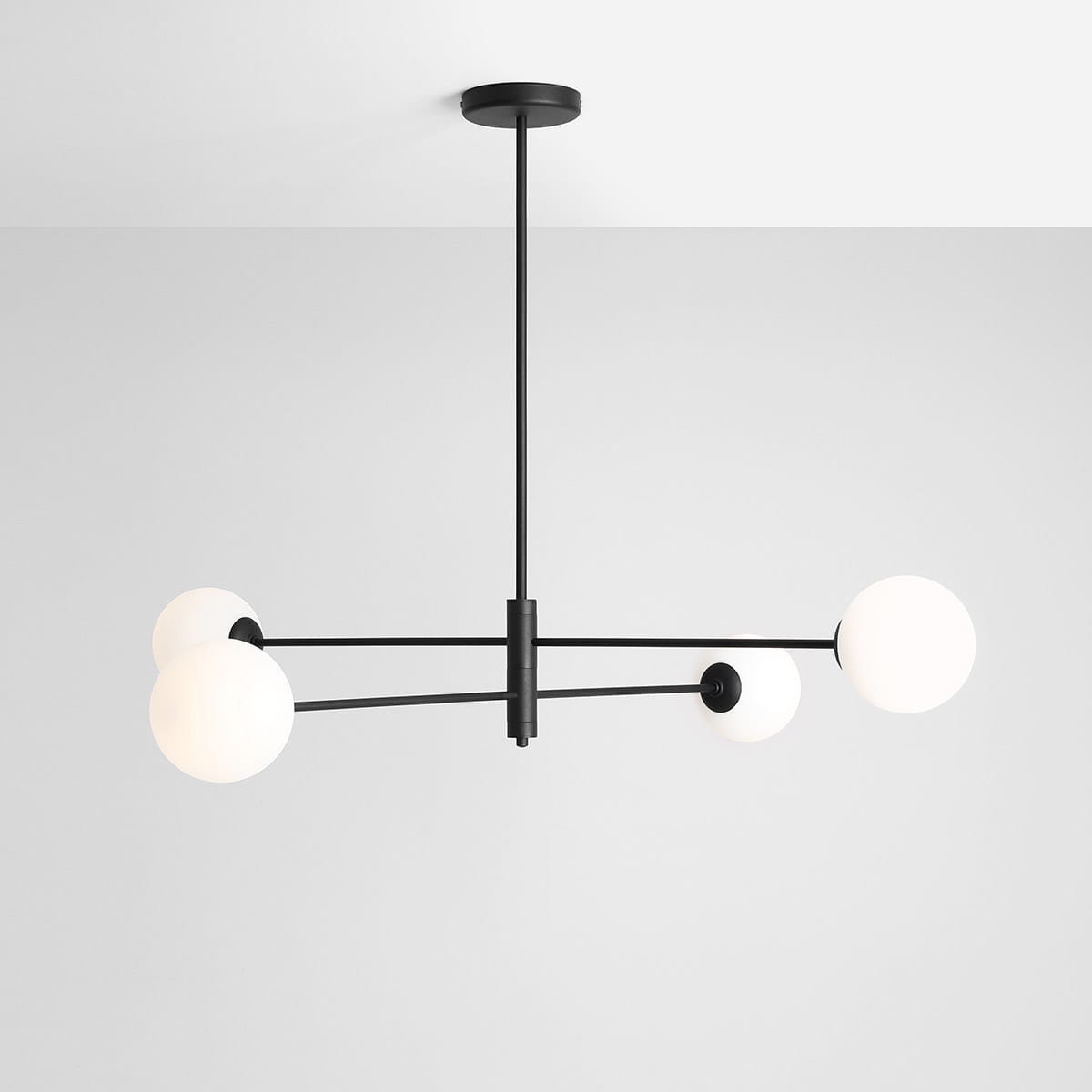 Lampa wisząca Homme czarna z czterema okrągłymi kloszami w białym kolorze, zawieszona na cienkich metalowych prętach, umieszczona na jasnym tle. Klosze równomiernie rozmieszczone, w formie prostokątnej konstrukcji.