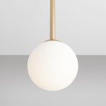 Lampa wisząca Pinne Short 1-punktowa w złotym kolorze, z białą, matową kulą. Ujęcie z bliska, ukazujące detal montażu. Prosta forma, zawieszona na cienkim przewodzie, na szarym tle. Idealna do nowoczesnych wnętrz.