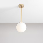 Lampa wisząca Pinne Short w złotym kolorze, z białym, okrągłym kloszem. Zamontowana na długim, złotym stelażu, wisi z sufitu na tle szarej ściany. Minimalistyczny design, idealna do nowoczesnych wnętrz.