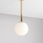 Lampa wisząca Pinne Short w złotym kolorze z białym, okrągłym kloszem, zawieszona na cienkiej, metalowej rurce. Ujęcie z góry, pokazujące elegancki design i gładką fakturę. Tło w jasnym odcieniu, co podkreśla wygląd lampy.