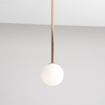 Lampa wisząca Pinne Medium w kolorze złotym, z białym, okrągłym kloszem. Montowana na długim, cienkim stelażu. Klosz wykonany z matowego szkła, zawieszony w centralnej pozycji, na jednolitym, jasnym tle.