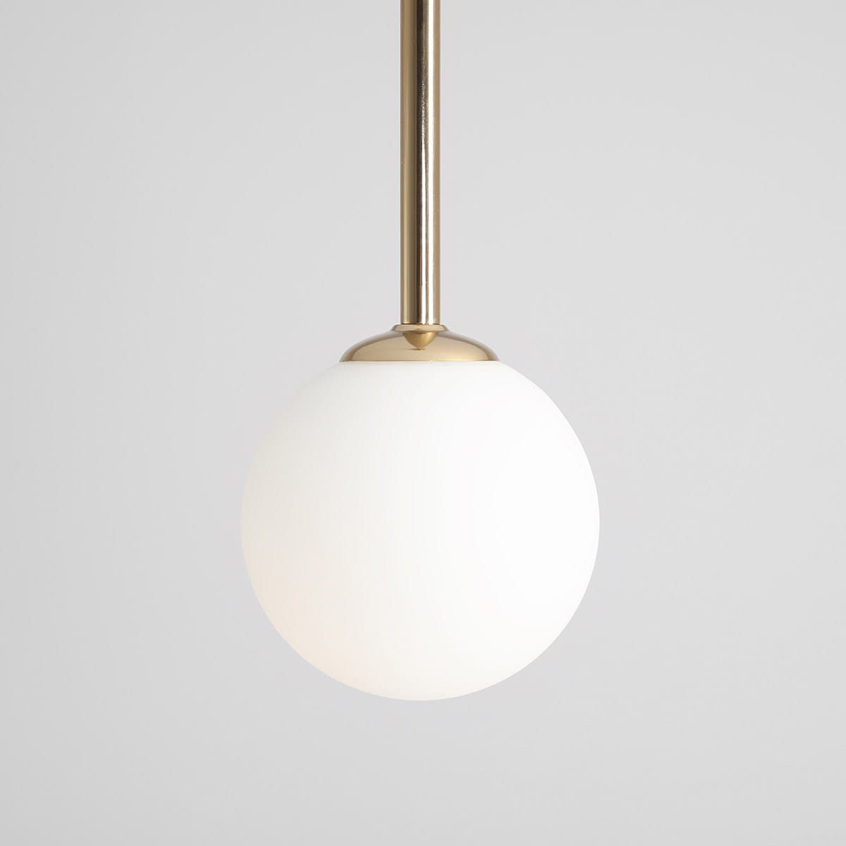 Lampa wisząca Pinne Medium w kolorze złotym z białym, okrągłym kloszem. Produkt zawieszony na cienkiej rurze, z widoczną metalową podstawą. Minimalistyczny design, idealny do nowoczesnych wnętrz. Tło proste, szare.