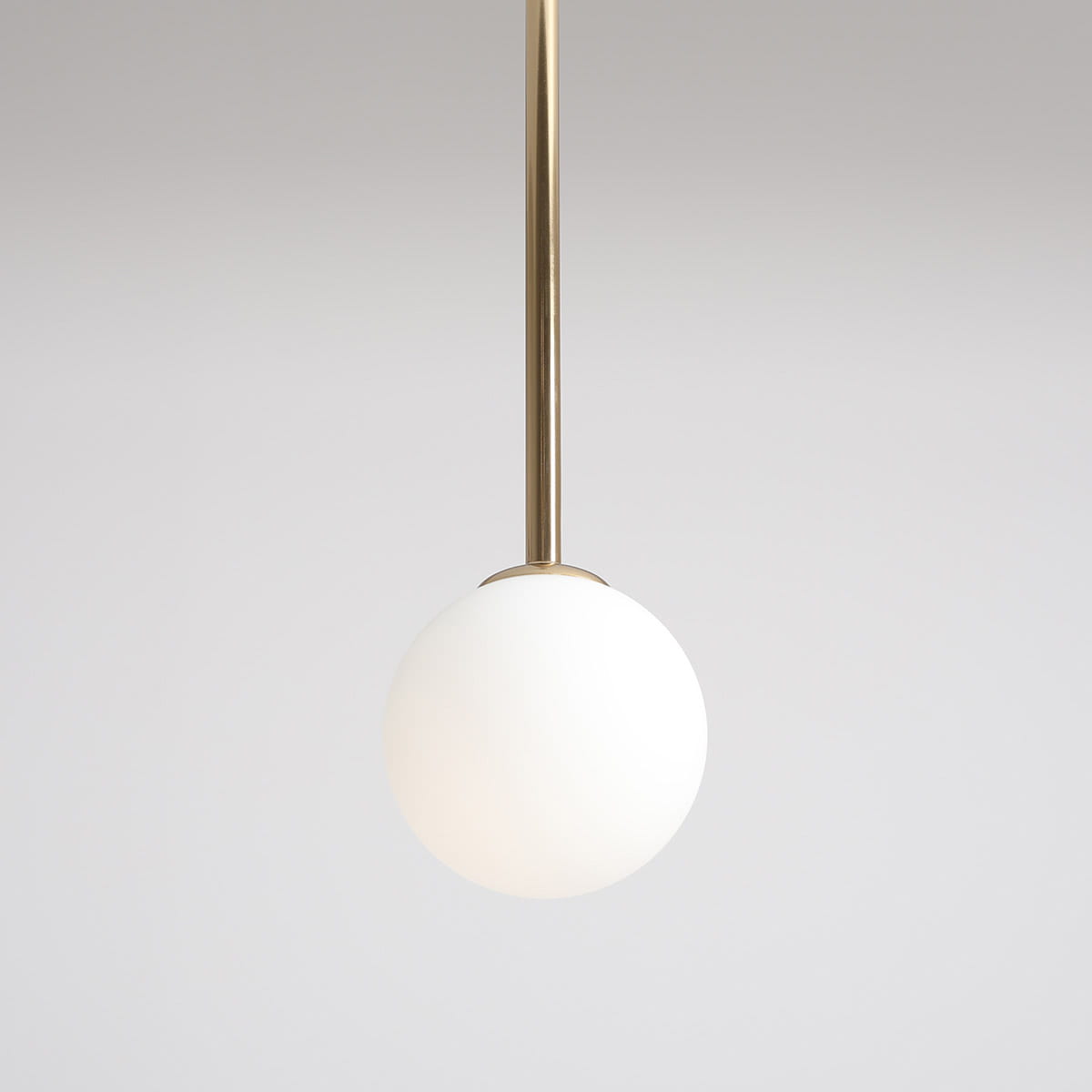 Lampa wisząca Pinne Long w kolorze złotym z białym, okrągłym kloszem z matowego szkła. Ujęcie z góry, zawieszona na cienkim, złotym stelażu, na jednolitym tle. Idealna do nowoczesnych wnętrz.
