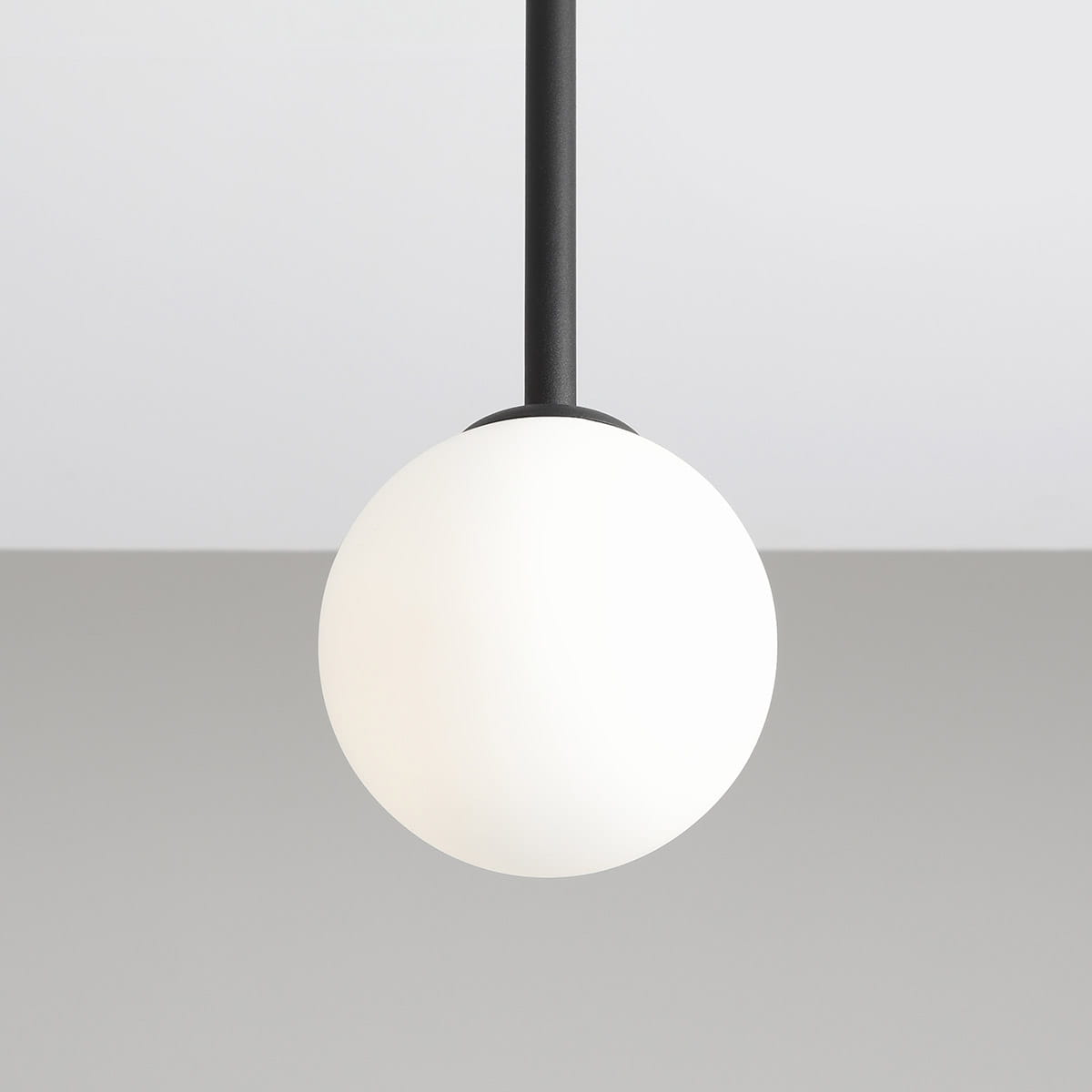 Lampa wisząca Pinne Short w kolorze czarnym, składająca się z metalowego ramienia i białej, matowej kulistej klosza. Produkt zawieszony pod kątem, na jednolitym tle, idealny do nowoczesnych wnętrz.