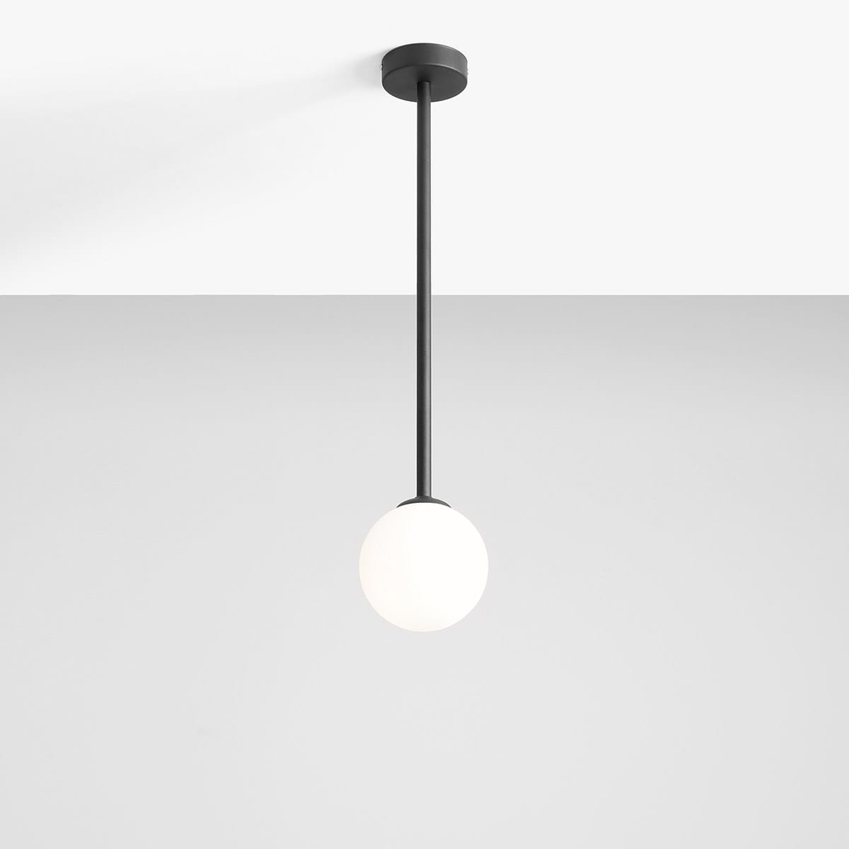 Lampa wisząca Pinne Medium z czarnym metalowym stelażem, zawieszona na długim, prostym kablu. Kulista, matowa oprawa w kolorze białym. Ujęcie frontalne, na jednolitym tle. Idealna do nowoczesnych wnętrz.