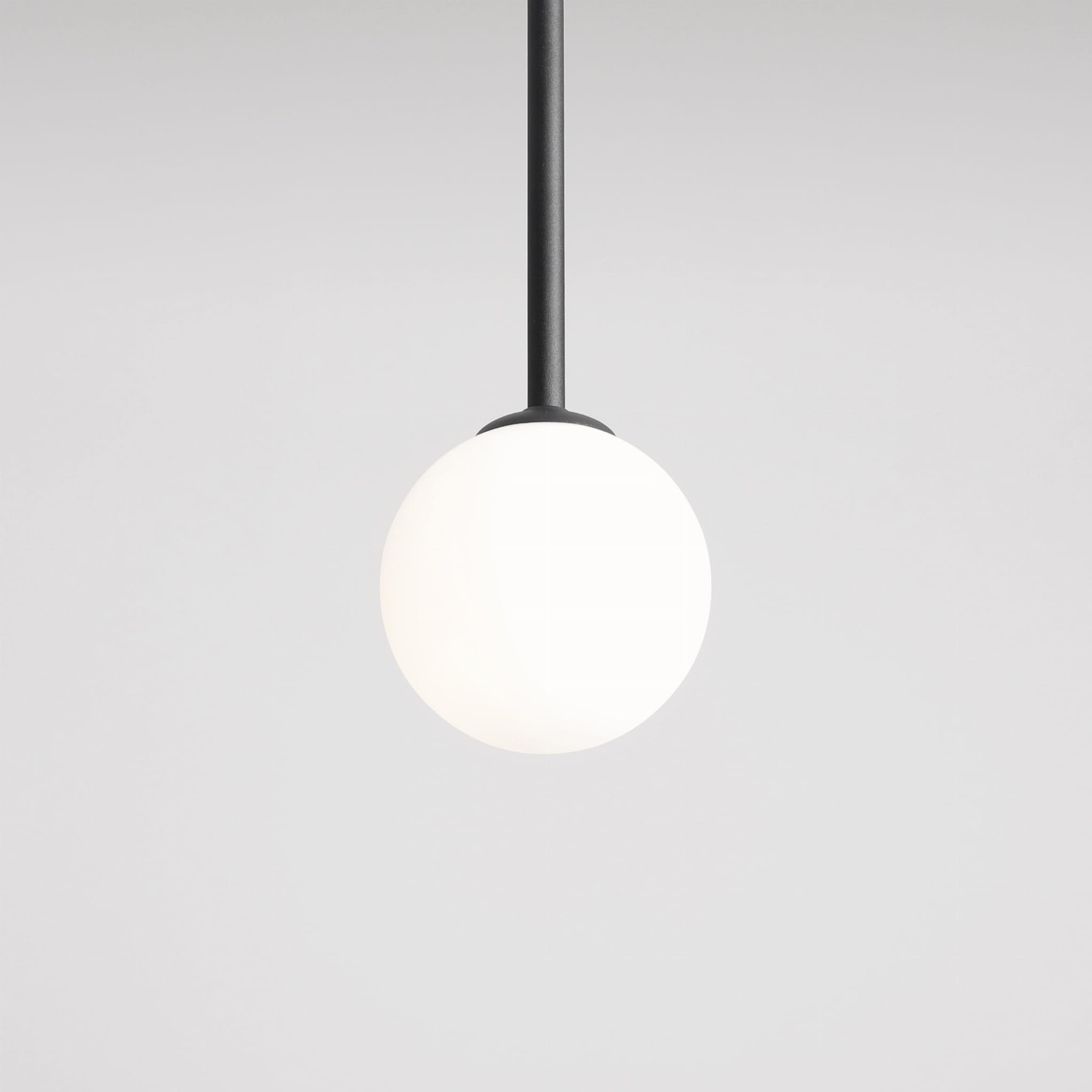 Lampa wisząca Pinne Medium w kolorze czarnym z białym, okrągłym kloszem. Zawieszona na cienkim, prostym przewodzie, prezentuje minimalistyczny design. Klosz wykonany z matowego szkła, umieszczony na metalowym uchwycie. Tło jasne, jednolite.