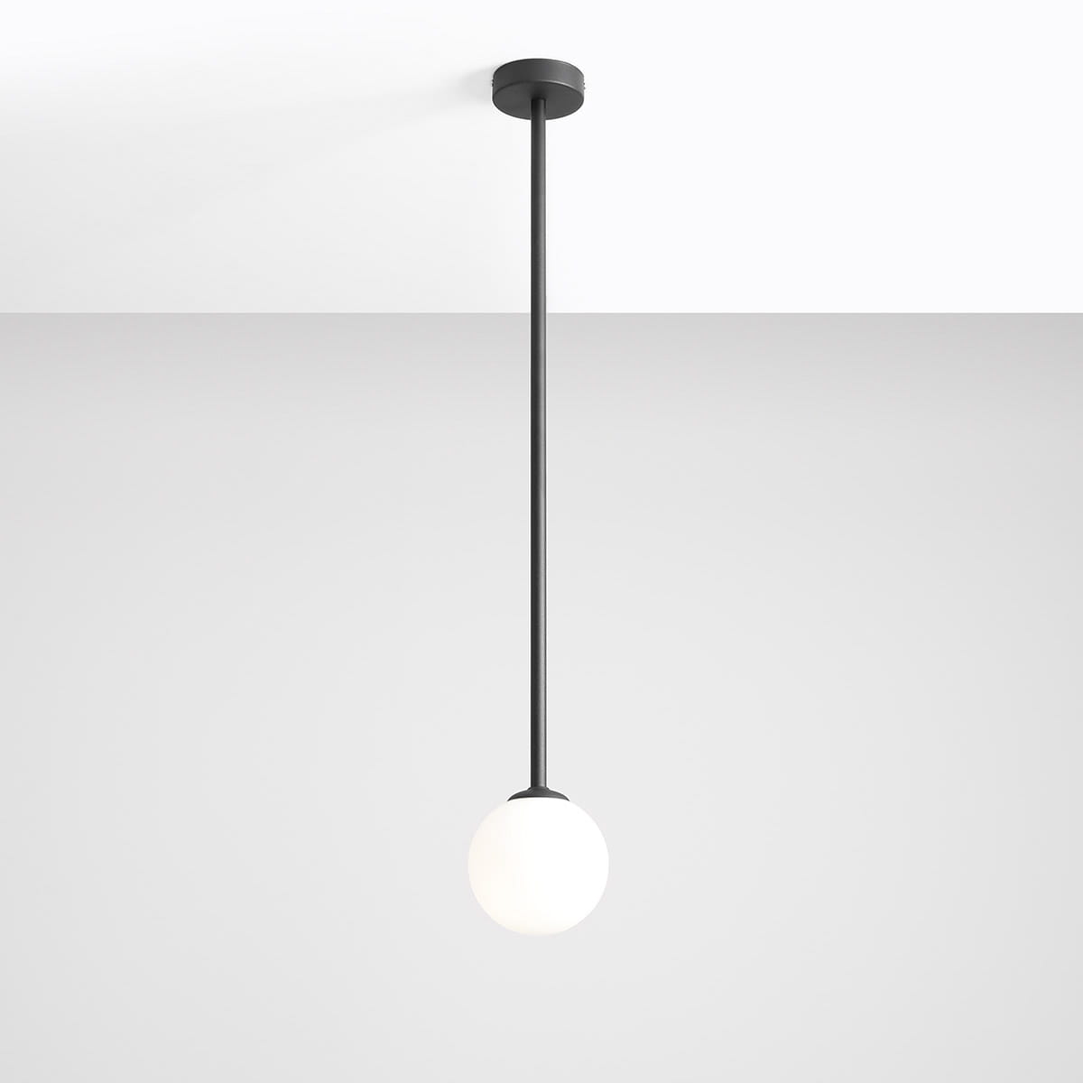 Lampa wisząca Pinne Long w kolorze czarnym, z długim metalowym przewodem i okrągłym kloszem z białego szkła. Ujęcie frontalne, pokazujące lampę zawieszoną na suficie, na jednolitym jasnym tle.