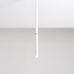 Biała lampa sufitowa Stick M, jednopunktowa, o cylindrycznym kształcie. Zawieszona centralnie, z widocznym źródłem światła na końcu. Tło jasne, minimalistyczne, podkreślające nowoczesny design lampy.