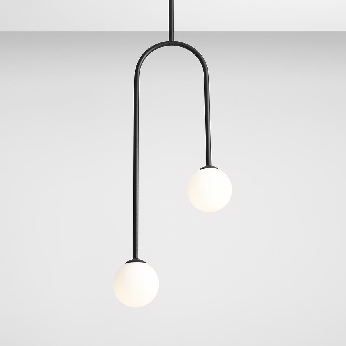 Lampa wisząca 2-punktowa Nave w kolorze czarnym, z dwoma okrągłymi kloszami w odcieniu białym. Ujęcie frontalne, produkt zawieszony na cienkim, zakrzywionym przewodzie, na jednolitym, jasnym tle.