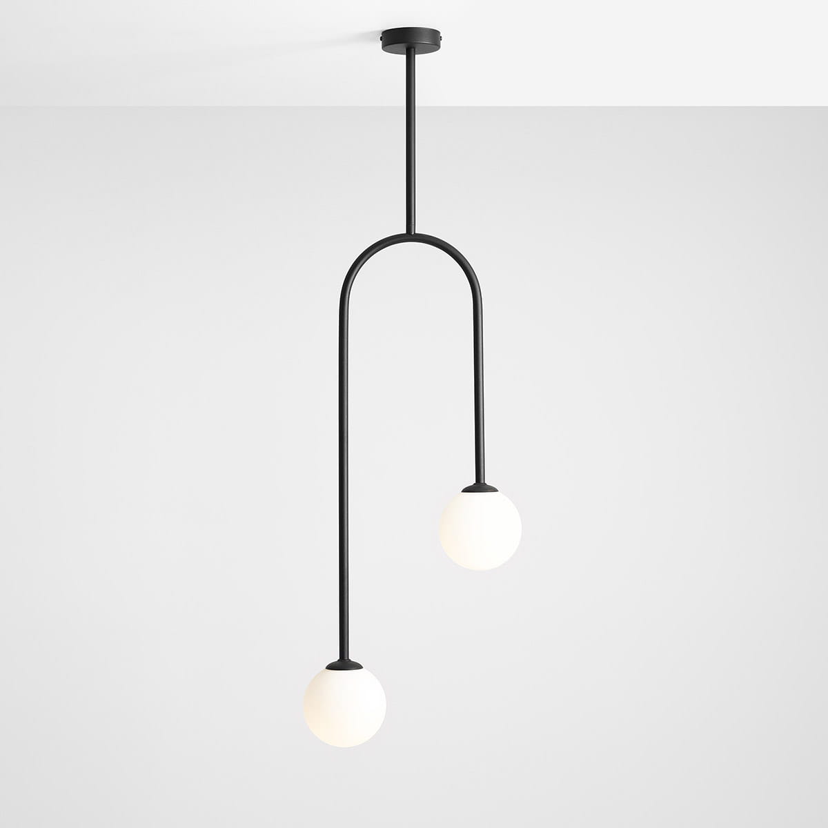 Lampa wisząca Nave w kolorze czarnym, 2-punktowa, z metalowym stelażem i dwoma okrągłymi, białymi kloszami. Ułożona w pozycji wiszącej, zawieszona na prostym, cylindrycznym wsporniku. Tło proste, jasne.