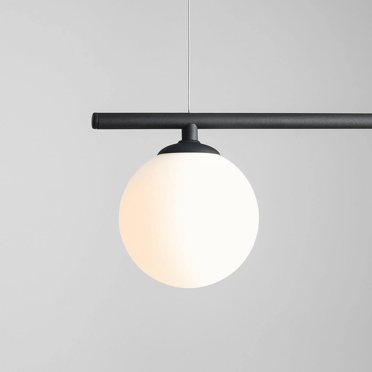 Czarna lampa wisząca Beryl Glass z trzema punktami świetlnymi, z matowym białym kloszem w kształcie kuli, zawieszona na prostym, czarnym stelażu. Ujęcie z boku, na szarym tle, podkreślające minimalistyczny design.