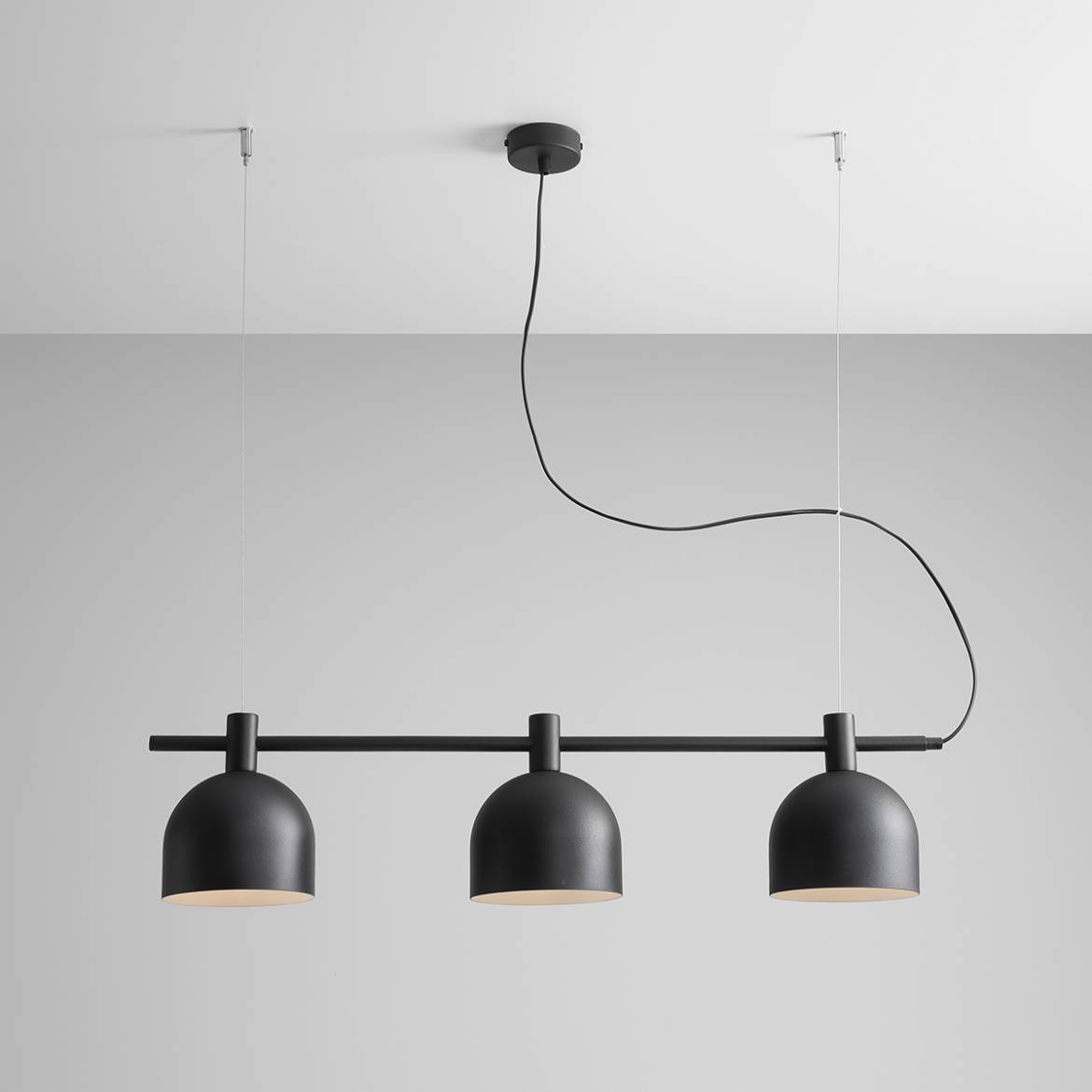 Lampa wisząca Beryl 3-punktowa o czarnym, matowym wykończeniu. Składa się z trzech okrągłych kloszy zawieszonych na poziomej metalowej rurze. Ujęcie z dołu, wisząca konstrukcja z widocznym kablem. Tło jasnoszare, minimalistyczne.