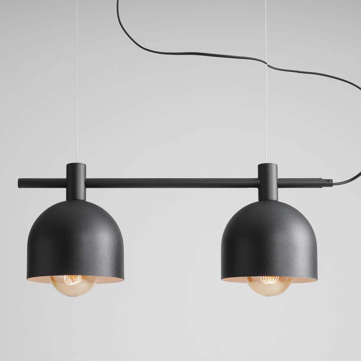 Czarna lampa wisząca Beryl z dwoma punktami świetlnymi, umieszczona na poziomej rurze. Klosze mają półkulisty kształt i matowe wykończenie. Lampa zawieszona na cienkim przewodzie, na tle jednolitej, jasnej powierzchni.
