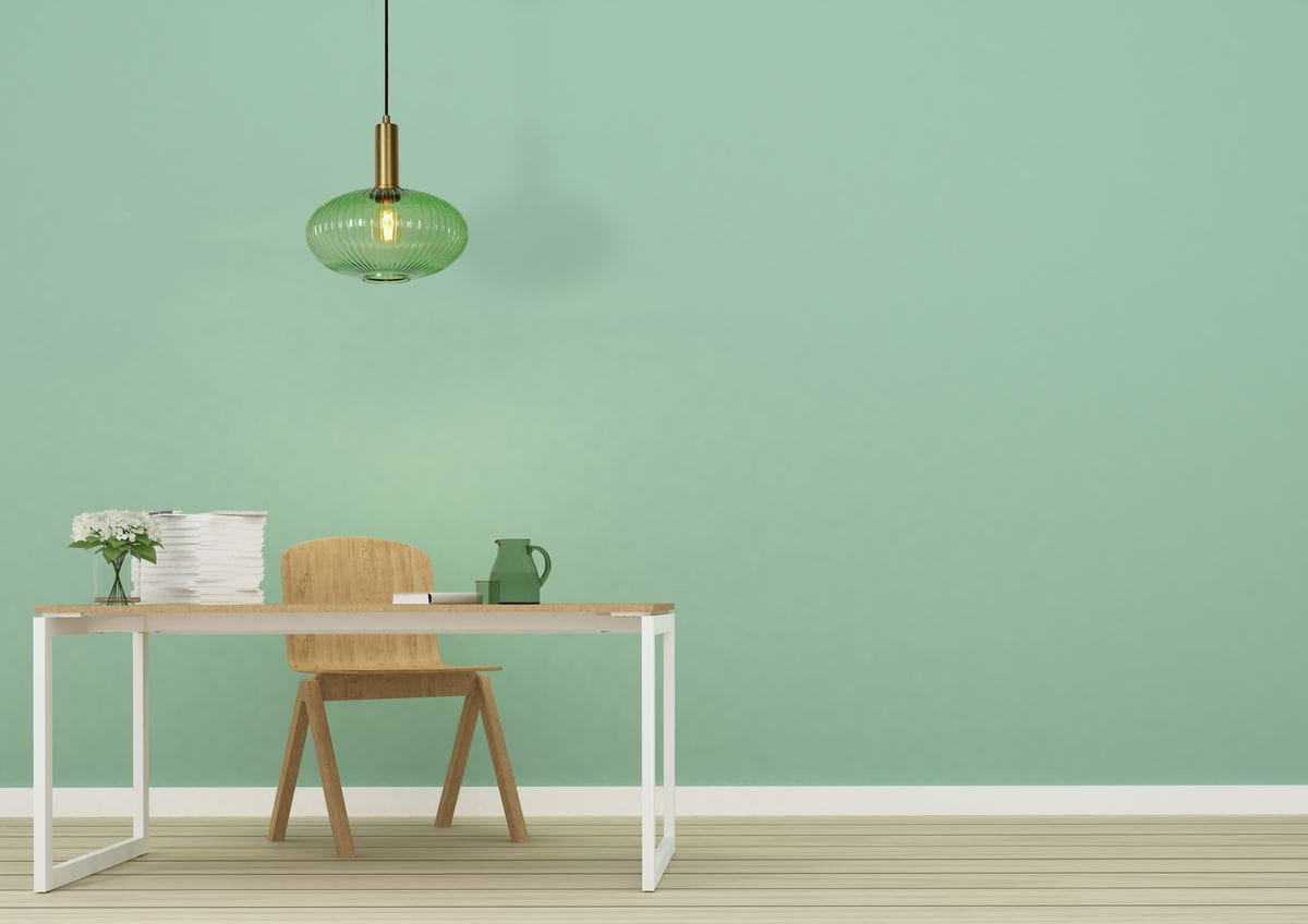 Lampa wisząca Maloto 1-punktowa w kolorze zielonym z mosiężnym uchwytem. Okrągły klosz z fakturowanego szkła wisi nad drewnianym biurkiem. Tło w odcieniu mięty, na stole widoczne akcesoria biurowe oraz kwiat w wazonie.