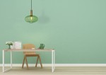 Lampa wisząca Maloto 1-punktowa w kolorze zielonym z mosiężnym uchwytem. Okrągły klosz z fakturowanego szkła wisi nad drewnianym biurkiem. Tło w odcieniu mięty, na stole widoczne akcesoria biurowe oraz kwiat w wazonie.