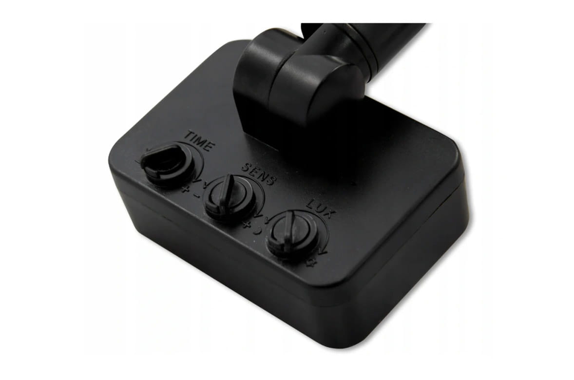 Naświetlacz LED halogen z czujnikiem ruchu, widok z góry na czarną podstawę z trzema pokrętłami: TIME, SENS i LUX. Pokrętła są oznaczone symbolami + i -, co sugeruje regulację ustawień. Produkt ma prostokątny kształt i jest zamontowany na uchwycie.