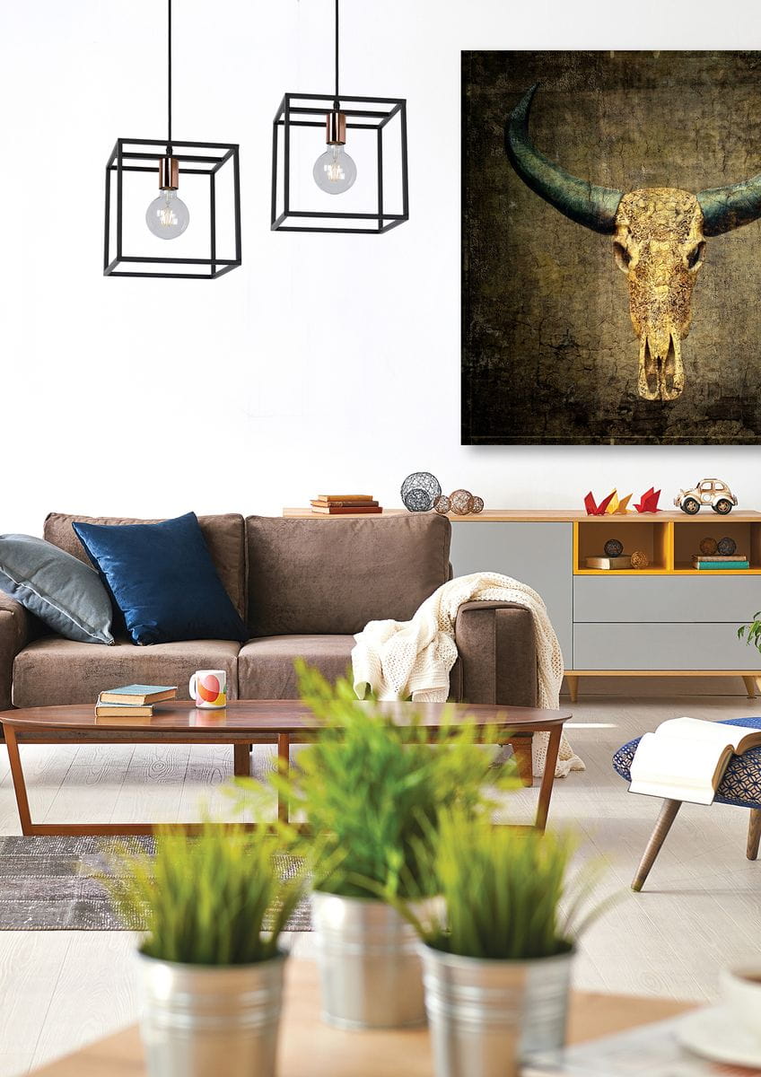 Czarna lampa wisząca Arthur 1-punktowa z metalową konstrukcją w formie sześcianu, z widoczną żarówką. Lampa zawieszona w nowoczesnym wnętrzu, w tle kanapa i dekoracje, na jasnym tle. Idealna do aranżacji przestrzeni.