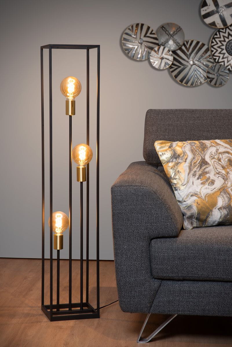 Czarna lampa podłogowa Ruben z trzema punktami świetlnymi, umieszczona obok szarej sofy. Otwarty, prostokątny stelaż z metalowymi detalami w kolorze złotym. Widoczna tekstura materiału sofy oraz dekoracyjna poduszka w odcieniach złota i beżu.