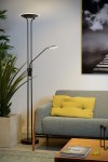 Czarna lampa podłogowa Champion LED z dwoma punktami świetlnymi. Górna lampa okrągła, niższa z ruchomym ramieniem. Stoi obok szarej kanapy z żółtą poduszką. Tło jasne, z rośliną i obrazem na ścianie.