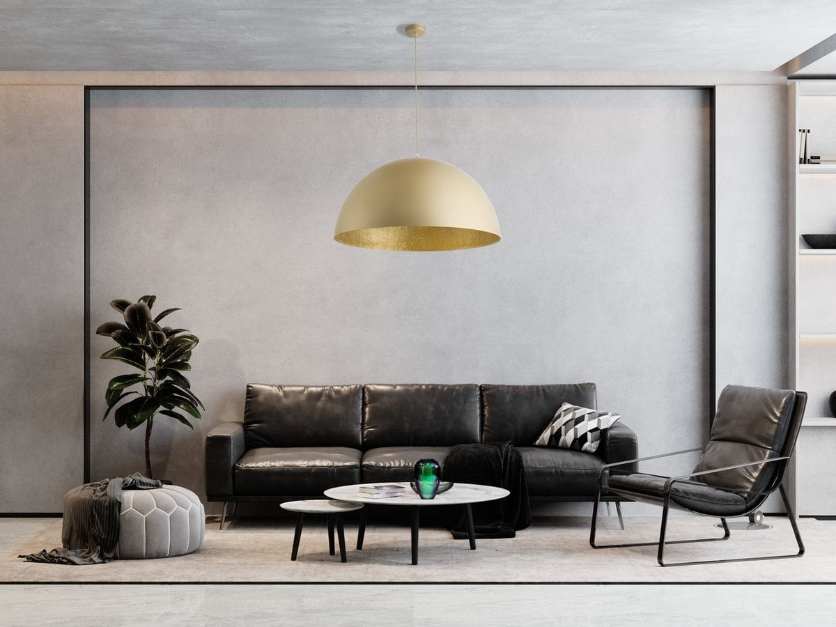 Złota lampa wisząca Sfera D50, okrągła, z matowym wykończeniem, zawieszona nad okrągłym stołem w nowoczesnym wnętrzu. W tle czarna sofa, roślina doniczkowa oraz dekoracyjne elementy, na jasnym tle.