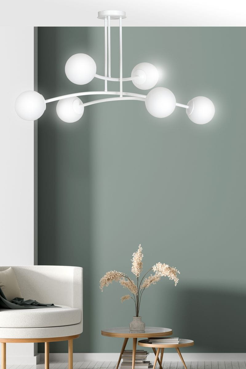 Lampa wisząca Halldor 6-punktowa w kolorze białym z sześcioma okrągłymi kloszami umieszczonymi na łukowatych ramionach. Ujęcie frontalne, lampa zawieszona na suficie, w tle stonowana zielona ściana i meble w nowoczesnym stylu.