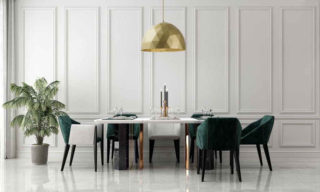 Złota lampa wisząca Diament D50 w kształcie geometrycznym, umieszczona nad białym stołem w jadalni. W tle widoczne zielone krzesła oraz roślina w doniczce. Ściany białe, gładkie, bez wzorów. Oświetlenie tworzy nowoczesny, elegancki klimat.