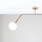 Lampa sufitowa Pure 2-punktowa w kolorze złotym, z dwoma okrągłymi kloszami, umieszczona na długim, zakrzywionym ramieniu. Klosze mają białą, matową powierzchnię, a lampa jest zamontowana na suficie. Tło w odcieniu jasnoszarym.