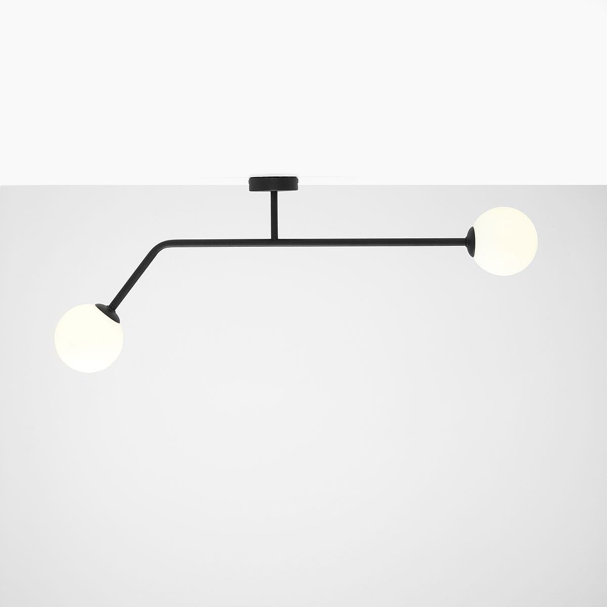 Czarna lampa sufitowa 2-punktowa Pure 2, z dwiema okrągłymi, białymi kulami w kształcie lamp, umieszczona na wygiętej metalowej konstrukcji. Widok frontalny, zawieszona na suficie. Prosta, nowoczesna forma.
