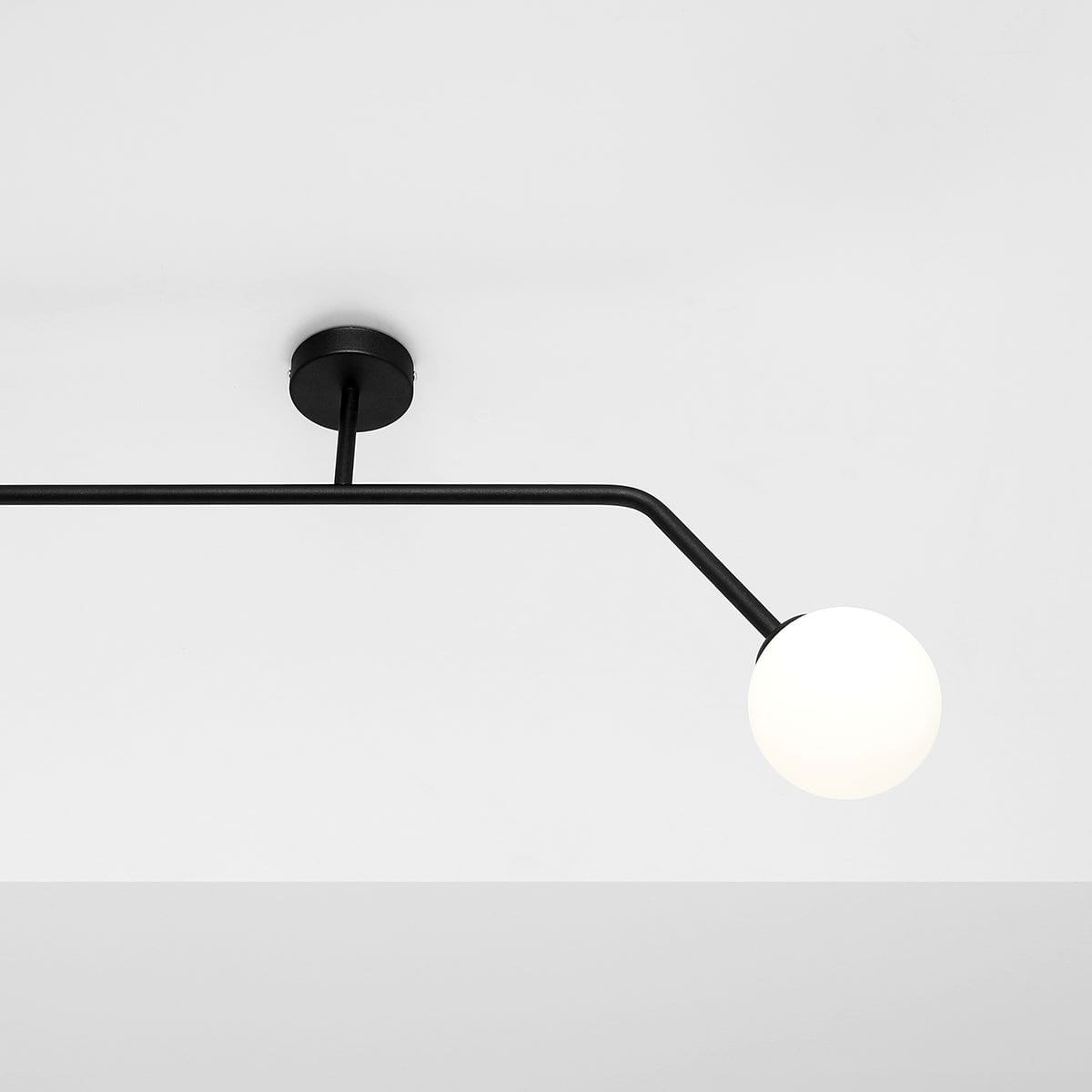 Czarna lampa sufitowa 2-punktowa Pure 1064D1_2. Składa się z metalowej, prostokątnej ramy oraz dwóch okrągłych, białych kloszy. Ujęcie z góry, lampa zamontowana na białym suficie. Kabel w kształcie litery L dodaje nowoczesnego charakteru.