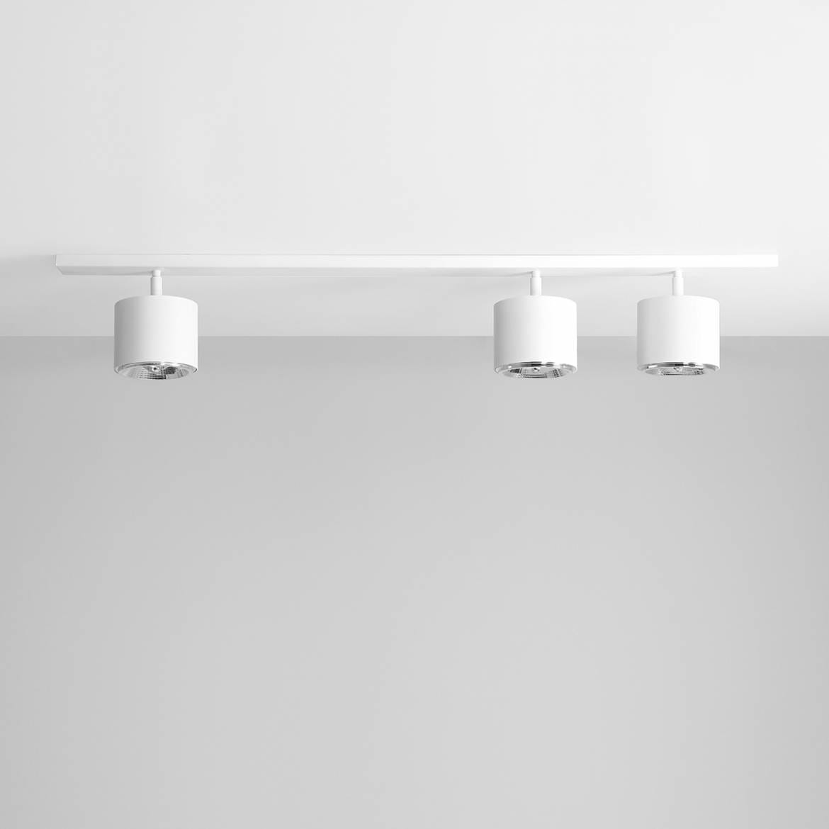 Biała lampa sufitowa 3-punktowa, składająca się z trzech cylindrycznych opraw oświetleniowych zamocowanych na prostej listwie. Ujęcie frontalne, na jednolitym tle. Lampa ma nowoczesny design i minimalistyczny styl.