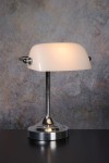 Lampa biurkowa Banker 1-punktowa w kolorze białym z chromowanym wykończeniem. Posiada okrągłą podstawę, prostą, chromowaną nogę oraz zaokrąglony klosz. Ujęcie frontalne, lampa leży na czarnym blacie, tło w odcieniach szarości.