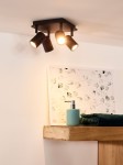Czarna lampa sufitowa Lennert IP44, 4-punktowa, z czterema reflektorami ustawionymi na kwadratowej podstawie. Reflektory skierowane w różne strony, umieszczone na tle jasnej ściany. W tle widoczna półka z zielonym ręcznikiem i butelką.