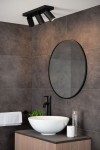 Czarna lampa sufitowa Taylor IP44, 3-punktowa, zamontowana na suficie. Reflektory w formie cylindrów skierowane w różnych kierunkach. W tle widoczna łazienka z okrągłym lustrem, umywalką i rośliną. Gładkie, ciemne płytki na ścianach.