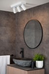 Lampa sufitowa Taylor IP44, 3-punktowa w kolorze białym, montowana na suficie. Klosze w formie cylindrów skierowane w różne strony. W tle widać okrągłe lustro oraz umywalkę z kamienia. Otoczenie w nowoczesnym stylu, na szarym tle.
