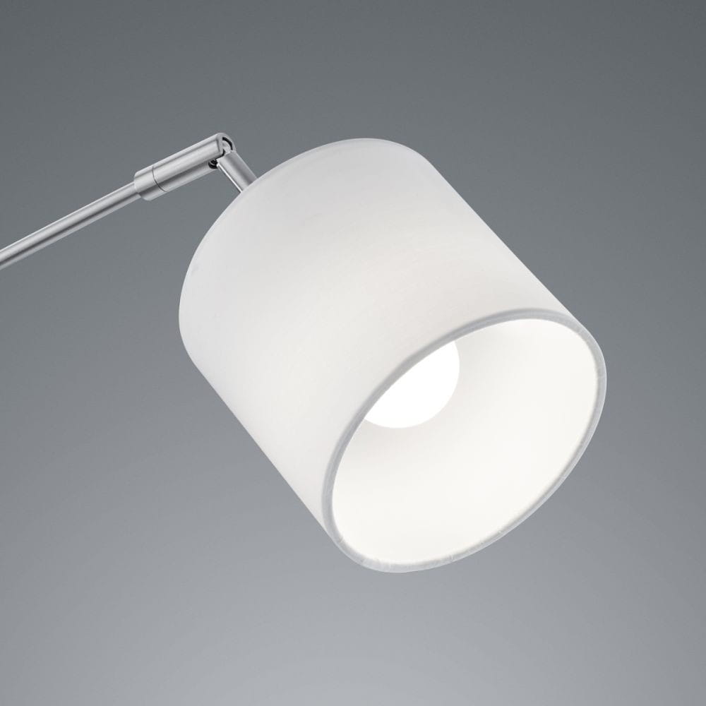 Lampa podłogowa Tommy 5-punktowa w kolorze niklowym. Widoczna biała oprawa w kształcie cylindra z wnętrzem emitującym światło. Ujęcie z góry, pokazujące detal klosza oraz ruchome ramiona lampy. Tło w odcieniu szarości.