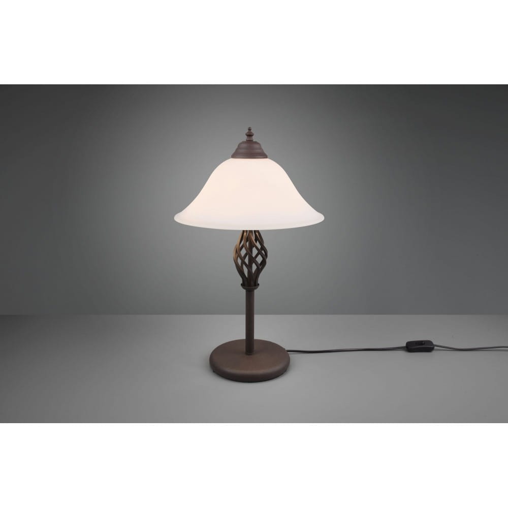 Brązowa lampa stołowa Rustica z dwoma punktami świetlnymi, z kloszem w kształcie dzwonu z mlecznego szkła. Wzór podstawy z plecionki, stojąca na okrągłej podstawie. Widoczny kabel z włącznikiem.