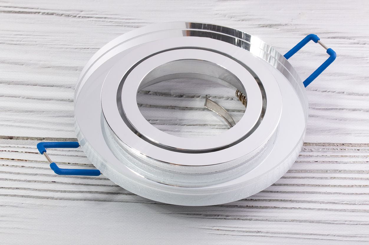 Oprawa oczko do zabudowy okrągła ruchoma GU10, w kolorze transparentnym, z metalowym obręczą w wykończeniu chromowanym. Ujęcie z góry, produkt leżący, z widocznymi niebieskimi zaczepami. Elementy montażowe są widoczne wewnątrz oprawy.