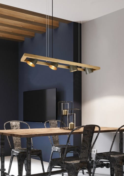 Lampa wisząca Bell 4-punktowa w kolorze antycznego niklu, z prostokątnym, metalowym korpusem i czterema regulowanymi źródłami światła. Zawieszona nad drewnianym stołem w nowoczesnym wnętrzu, na tle ciemnej ściany i telewizora.