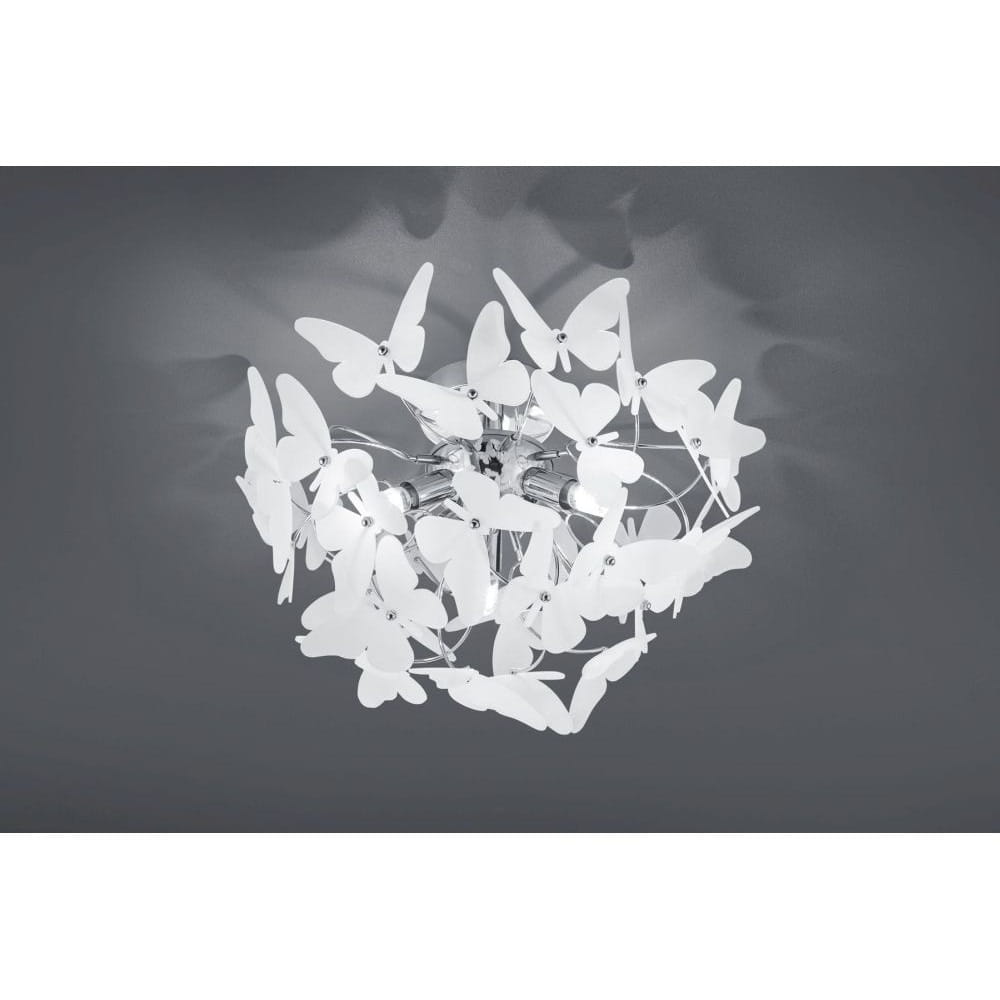 Lampa sufitowa Butterfly z trzema punktami świetlnymi, wykonana z chromu, zdobiona białymi, plastikowymi motylkami. Ujęcie z dołu, pokazujące detal konstrukcji oraz rozmieszczenie motyli. Tło w ciemnym kolorze, podkreślające efekt świetlny.