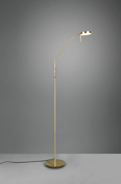 Lampa podłogowa Monza LED w kolorze mosiądzu, o smukłej, wygiętej konstrukcji z podstawą okrągłą. Główka lampy regulowana, umieszczona na długim stelażu, z widocznym przewodem zasilającym. Tło w odcieniach szarości.